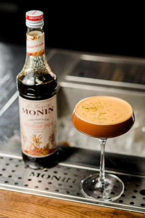 UKRAINE, KYIV - MARCH 12, 2021: angle view bottle of Monin muscovado sugar syrup and wineglass of tasty cocktailのeditorial素材