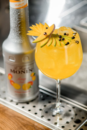 UKRAINE, KYIV - MARCH 12, 2021: Close-up of glass with bright drink decorated with slices of mango fruit and bottle of Monin brand nearbyのeditorial素材