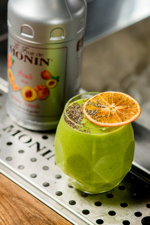 UKRAINE, KYIV - MARCH 12, 2021: Close-up of glass of green cocktail with chia seeds decorated by orange slice on and bottle of Monin brand nearbyのeditorial素材