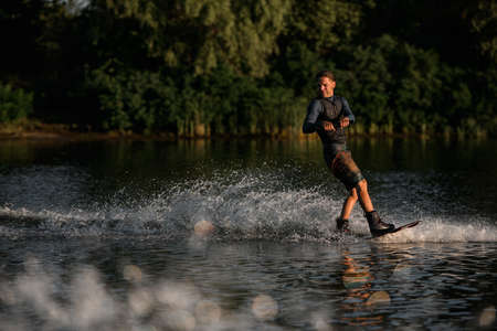 Active sportive man in wetsuit energetically balancing on water surface on wakeboardの写真素材