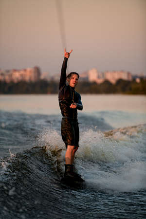 wakeboarder holds rope and rides down the wave and show surfer gesture.の写真素材