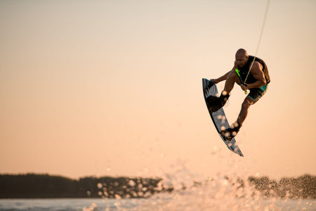 energy muscular sportsman making trick in jump time with wakeboard against the backdrop of the skyの写真素材