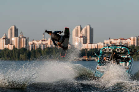wakeboarder moving fast behind boat holding rope and jumping and flips on splashing river wave.の写真素材