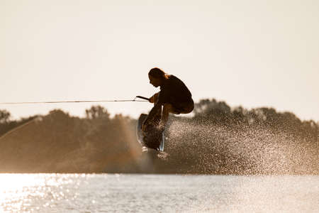 Close-up view of guy holding rope and skillfully jumping high with wakeboard over waterの写真素材