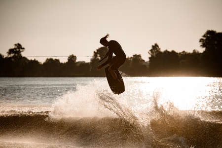 male wakeboarder masterfully jumping on wakeboard over splashing waveの写真素材