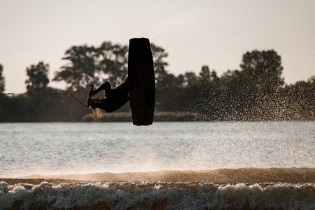 active male wakeboarder makes extreme stunts jumping and flips on wakeboard over splashing waterの写真素材