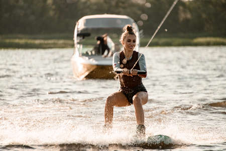 beautiful athletic woman on wakeboard rides on the water holding on to ropeの写真素材