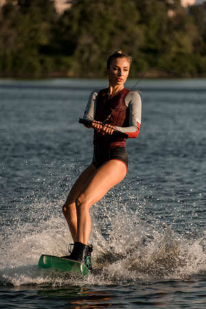 Beautiful woman holds rope and balancing on splashing water surface on wakesboard.の写真素材