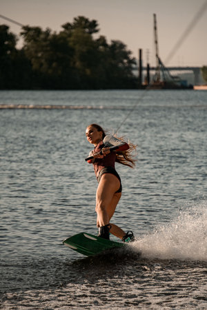 Beautiful active woman holds rope and balancing on wave on wakeboard.の写真素材