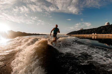 athletic man wakesurfer riding down the blue splashing wave on a warm dayの写真素材
