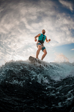 athletic man wakesurfer actively balancing on wakeboard along the river waveの写真素材
