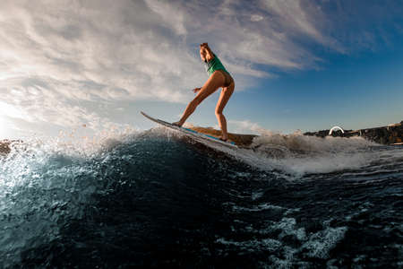 young attractive woman skilfully balances on splashing wave on wakesurfの写真素材