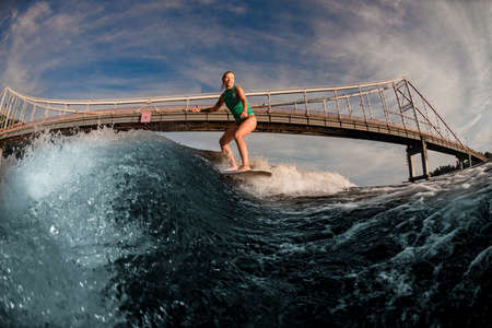 view of beautiful woman wakesurfer riding down on the board on splashing wave against bridge.の写真素材