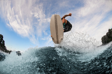beautiful view of a wakesurf board and man jumping in the air above a splashing wave