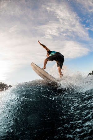 rear view of man balancing on wave on wakesurf board on splashing wave.の写真素材