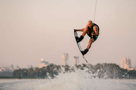 healthy strong man holds cable and skilfully making extreme jump showing trick on wakeboard.の写真素材