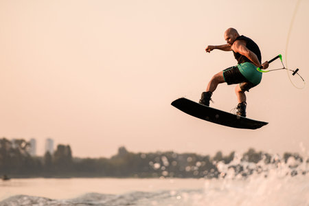 great view of active muscular man making trick and jump with wakeboard on sky background.