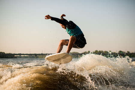 athlitic man energetically jumping on a wakesurf board over river wavesの写真素材
