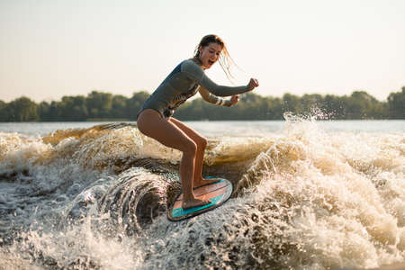 screaming wet woman wakesurfer riding on splashing wave on a warm dayの写真素材