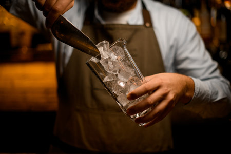 clear glass in bartender hand and pouring pieces of ice into it using steel scoop