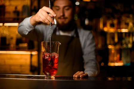 selective focus on hand of bartender stirring cocktail with a spoon in the mixing glass on the bar counterの写真素材