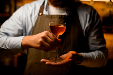 front view of wine glass with drink in hands of man bartender.の写真素材