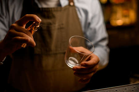 Close-up of hands of male bartender with empty transparent glass and and spray bottleの写真素材