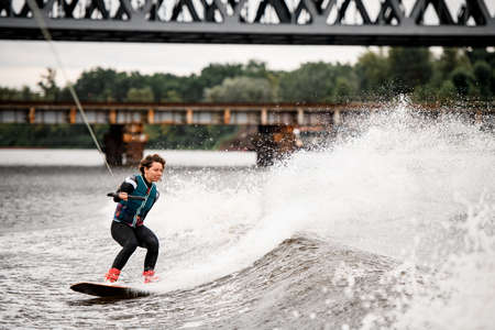 Young active woman riding wave on wakeboard holding rope with her handの写真素材