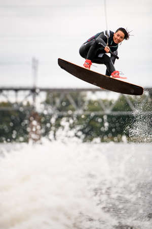 wakeboarder girl makes trick and jumping over the splashing river waveの写真素材