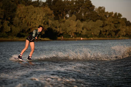 view of happy woman holds rope and masterfully riding wakeboard on splashing river water.の写真素材