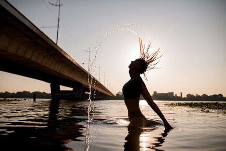 awesome silhouette of attractive fit woman in the water that shakes wet hairの写真素材