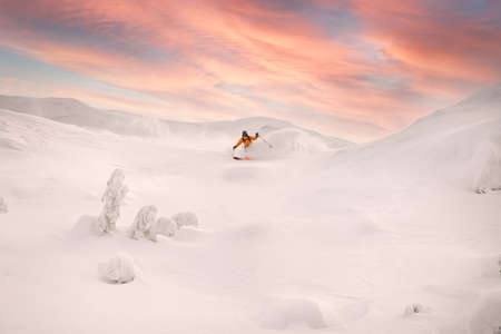 beautiful view of freeride skier skilfully rides down the mountain slope against colorful sky in background.の写真素材