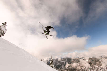 skier performs masterful jump in the air over snowy mountain slopeの写真素材