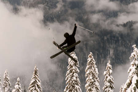 freeride skier performs jump in the air over a snow-covered mountain slopeの写真素材