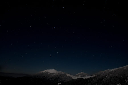 Dark night starry sky over mountain top covered with snow.の写真素材