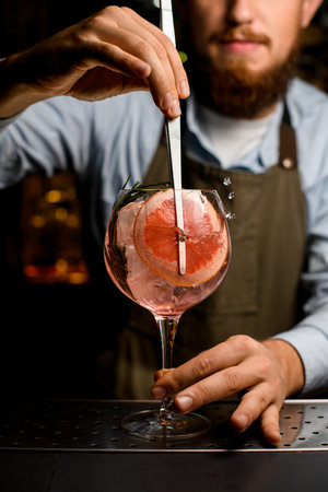 goblet glass with cold cocktail that the hand of barman decorating by fresh slice of grapefruit...