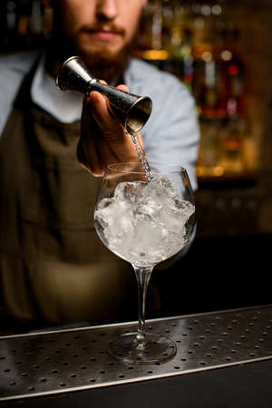 clear wine goblet glass in which bartender gently pours liquid from jiggerの写真素材