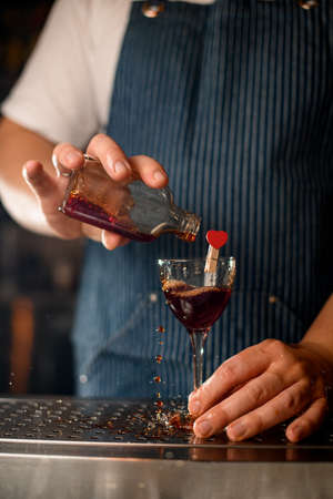 male hand holds wineglass decorated with heart and pours drink into itの写真素材