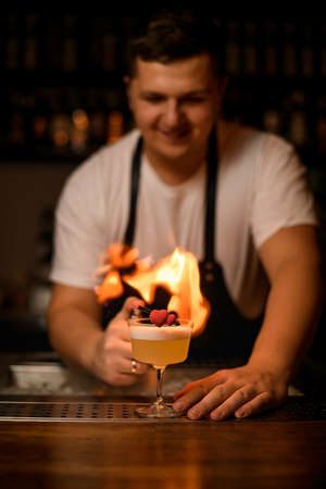 decorative heart on glass with foamy cocktail on the bar and male bartender with fire on backgroundの写真素材