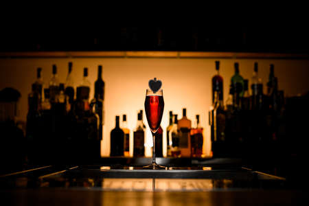 beautiful transparent wine glass with red cold alcoholic drink decorated with wooden heart on the bar counterの写真素材