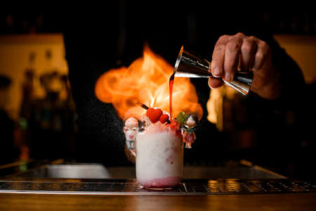 Bartender holds steel jigger in his hand and pours syrup into glass with cocktail decorated with small hearts.の写真素材