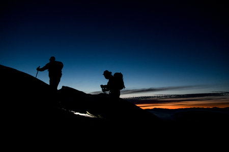 dark silhouettes of skiers climbing the mountain against the backdrop of evening skyの写真素材