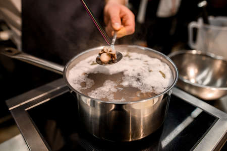 small boiled octopus in a spoon over pot of waterの写真素材