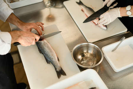 view of the table on which the hands of the chefs cut the fishの写真素材