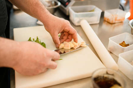 close-up on the hands of a man chef who neatly puts a vegetable on a knifeの写真素材