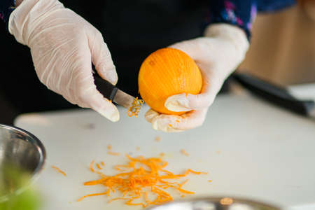 hands in gloves holds an orange and cuts off the peel from itの写真素材
