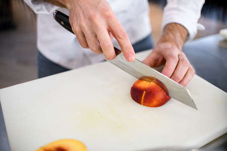 male hand cuts with knife ripe peach fruit on a white cutting boardの写真素材