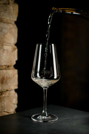 high wine glass into which white tasty sparkling wine is poured from a bottle.の写真素材