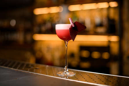 cocktail glass with foamy pink drink and decoration on blurred bar backgroundの写真素材