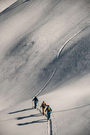 Beautiful aerial view of group of people walking at snowy trail at mountain slopeの写真素材